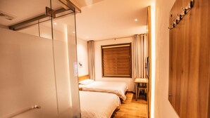 Een hotelkamer met twee bedden, een houten vloer, een raam met gordijnen en een houten garderobe.