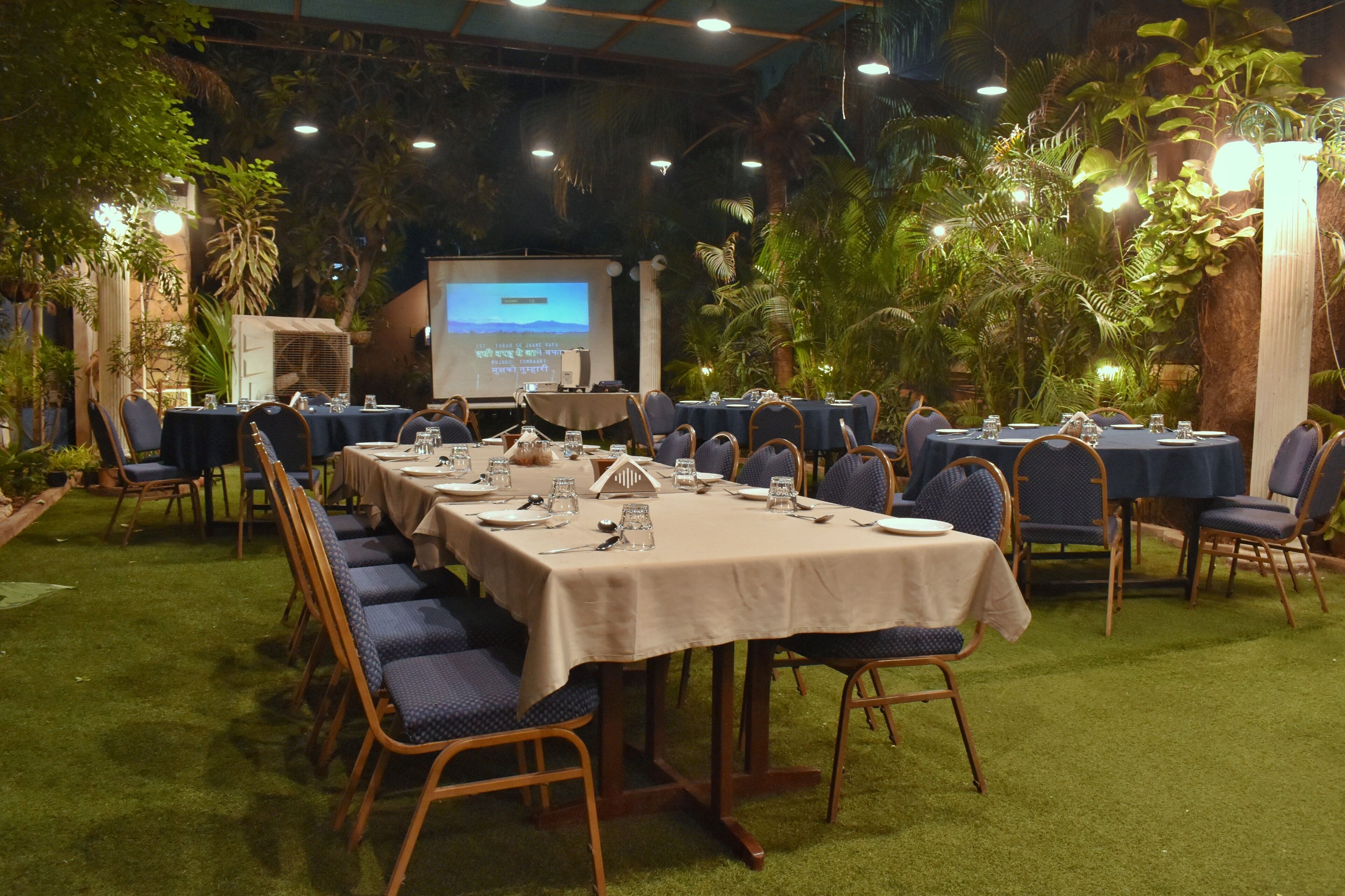 Une salle de conférence avec des tables disposées pour une réunion, entourée d’une végétation luxuriante et équipée d’un écran de projection.