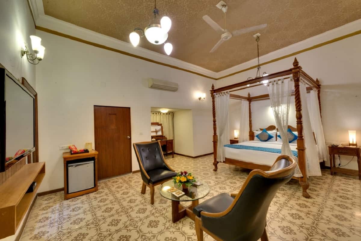A hotel room with a four-poster bed, a sitting area with a glass table, a ceiling fan, and a television.