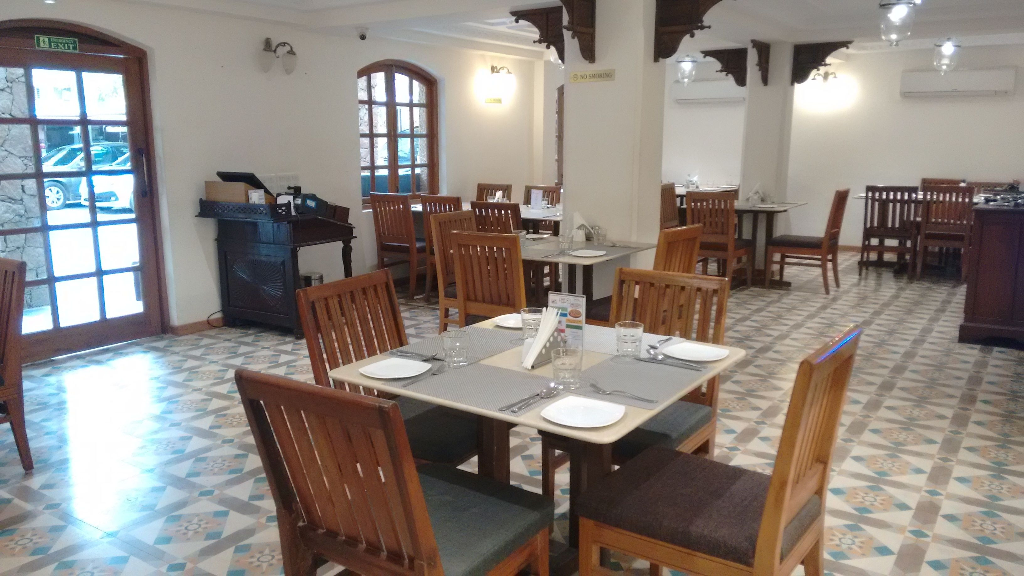A dining area with wooden tables and chairs, a tiled floor, and a view of the outside through a window.
