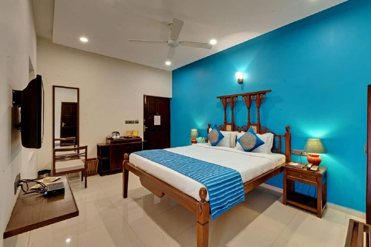 A bedroom with a bed, bedside tables, a desk, a mirror, a ceiling fan, and a blue accent wall.