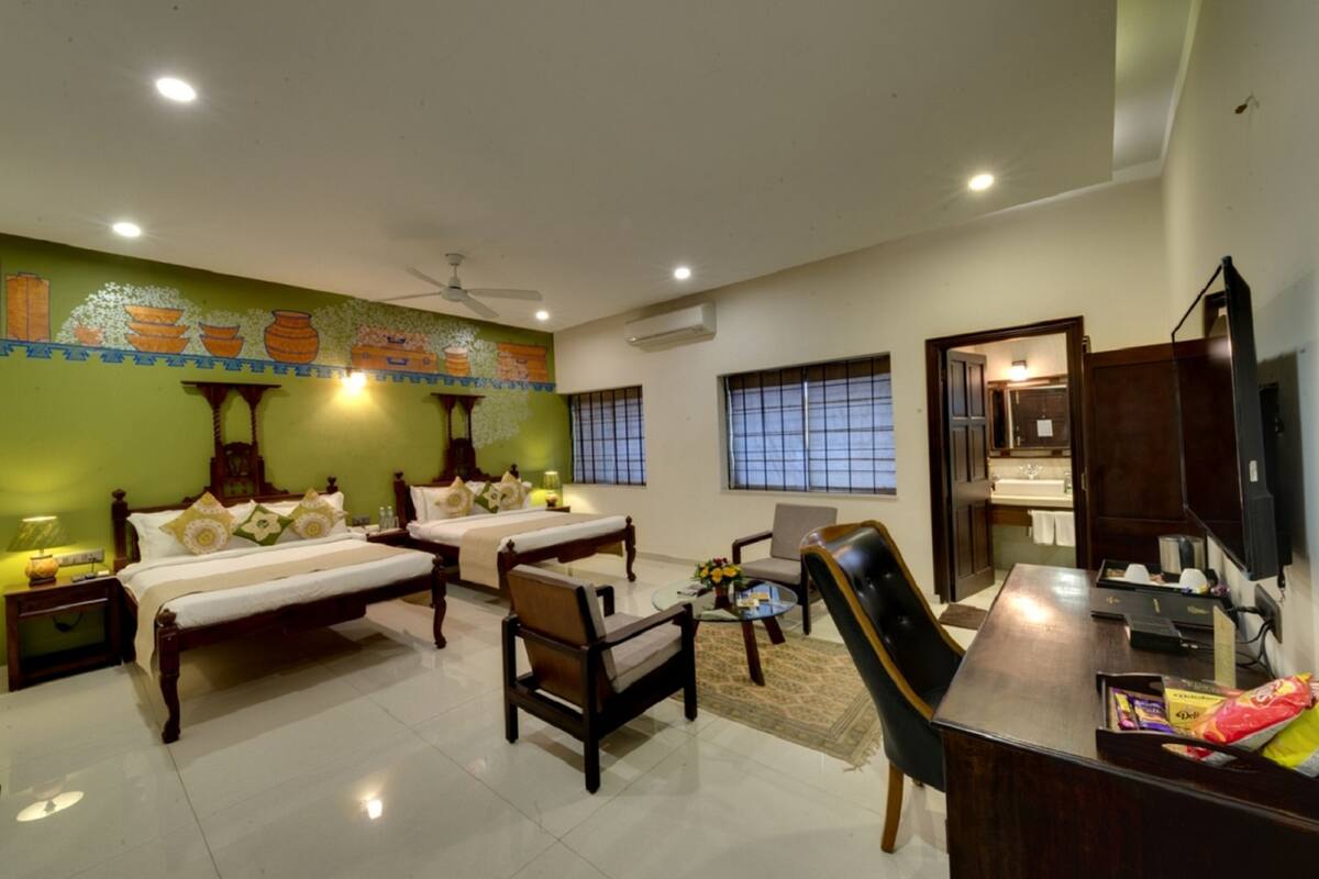 A hotel room with two beds, a desk, a chair, a television, and a bathroom visible through an open door.