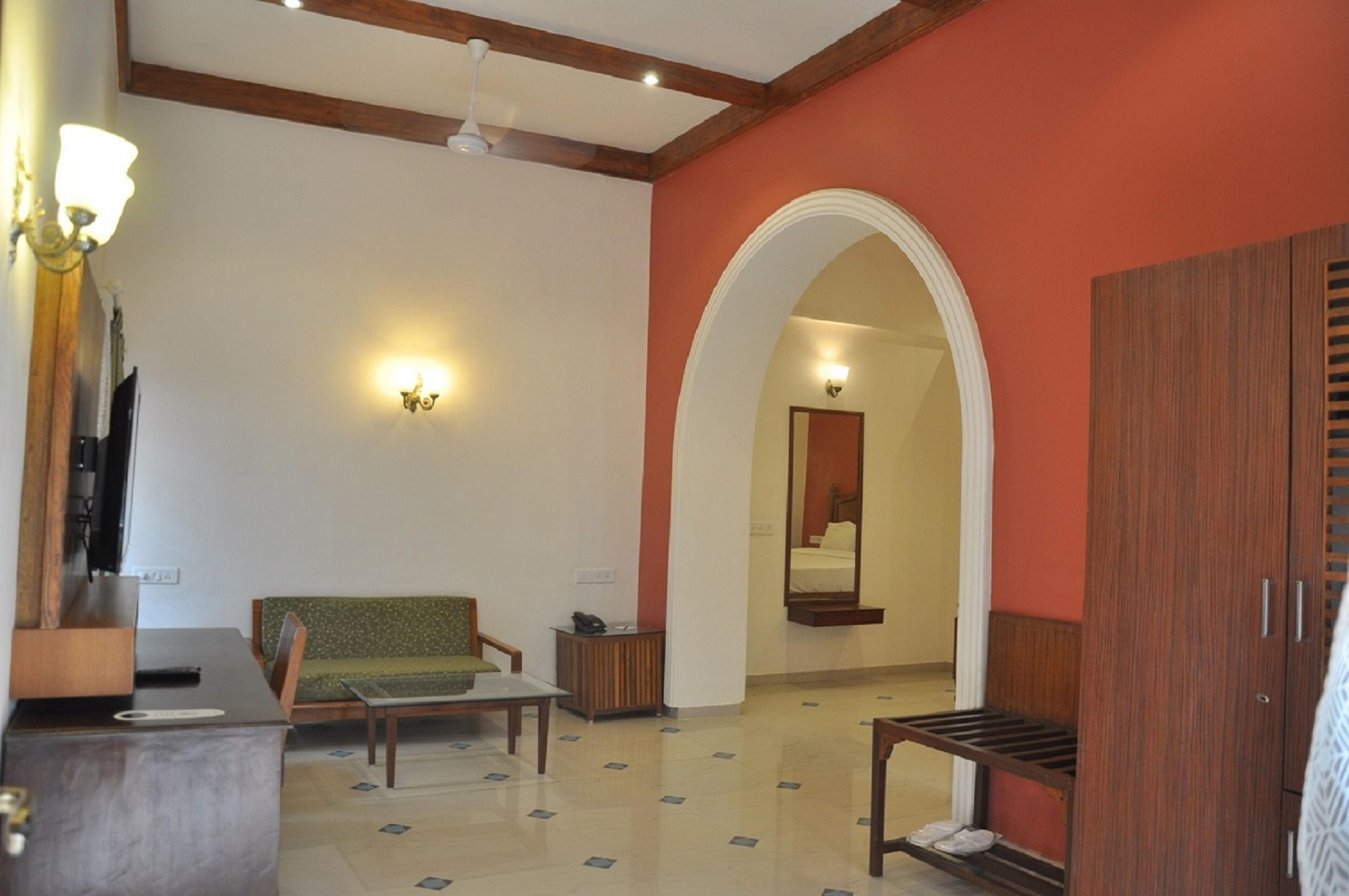 A hotel room with a sofa, a small table, a wooden cabinet, a mirror, and a wardrobe.