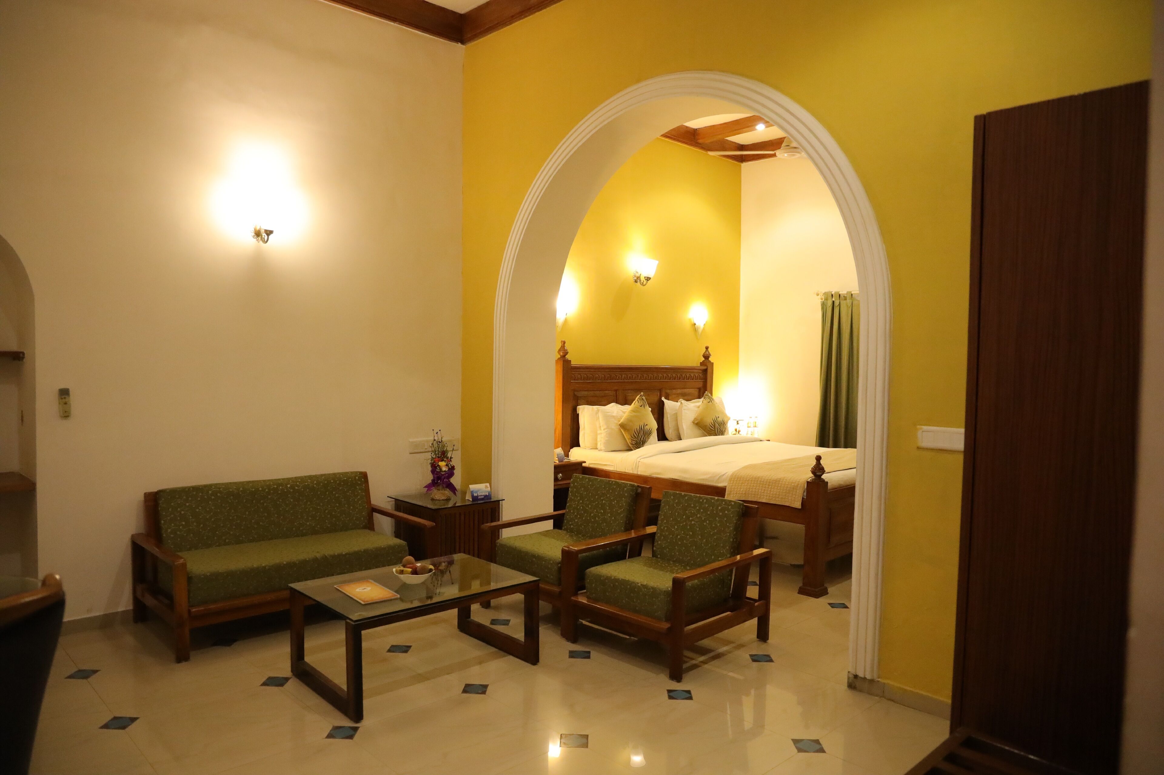 A hotel room with a sofa, armchairs, a coffee table, a bed, and a nightstand.