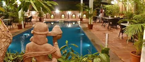 An outdoor swimming pool area with a statue, potted plants, and tables and chairs.