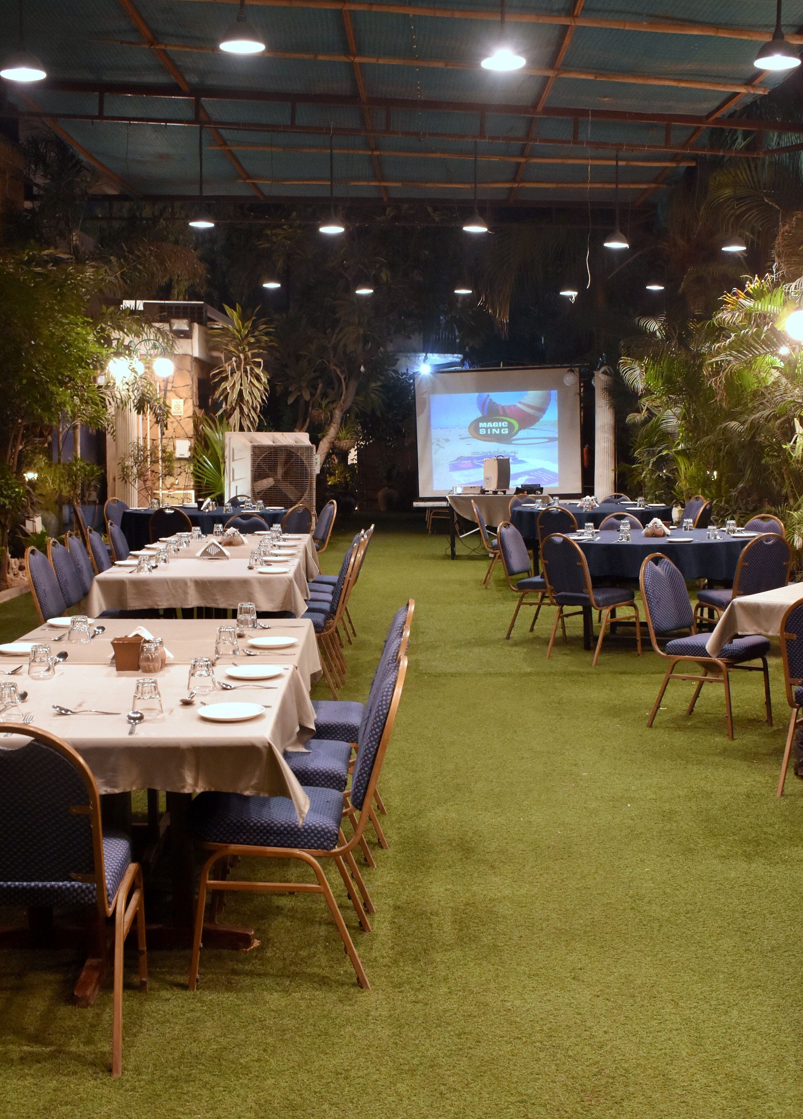 A banquet hall with tables set for dining, a projector screen displaying 'MAGIC SING', and ambient lighting.