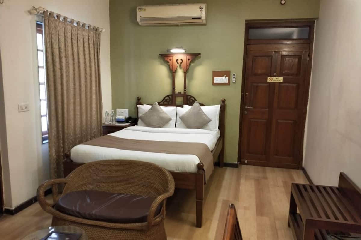 A bedroom with a bed, a chair, a bedside table, an air conditioning unit, and a door.