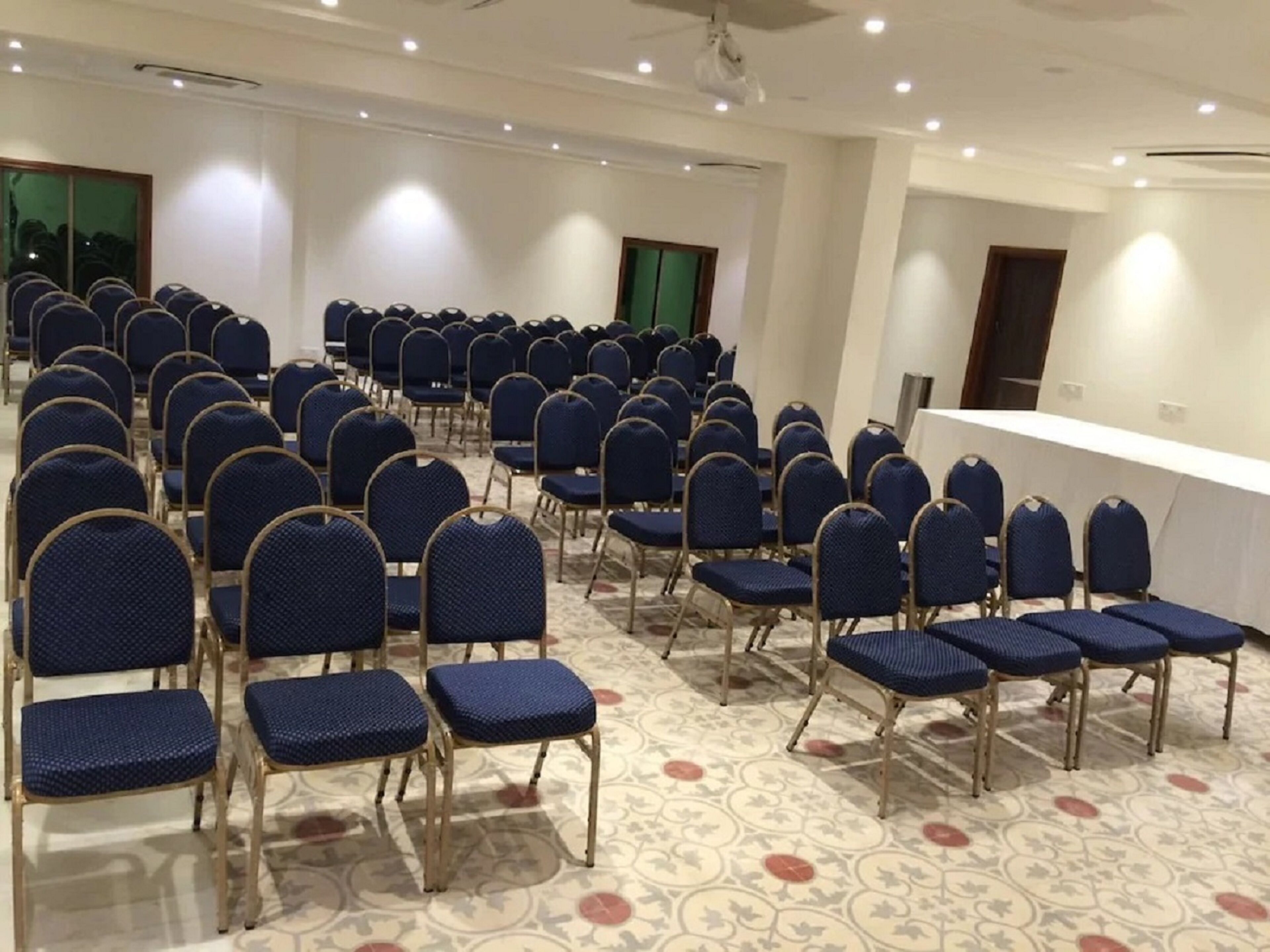 A conference room with rows of blue chairs and a white table.