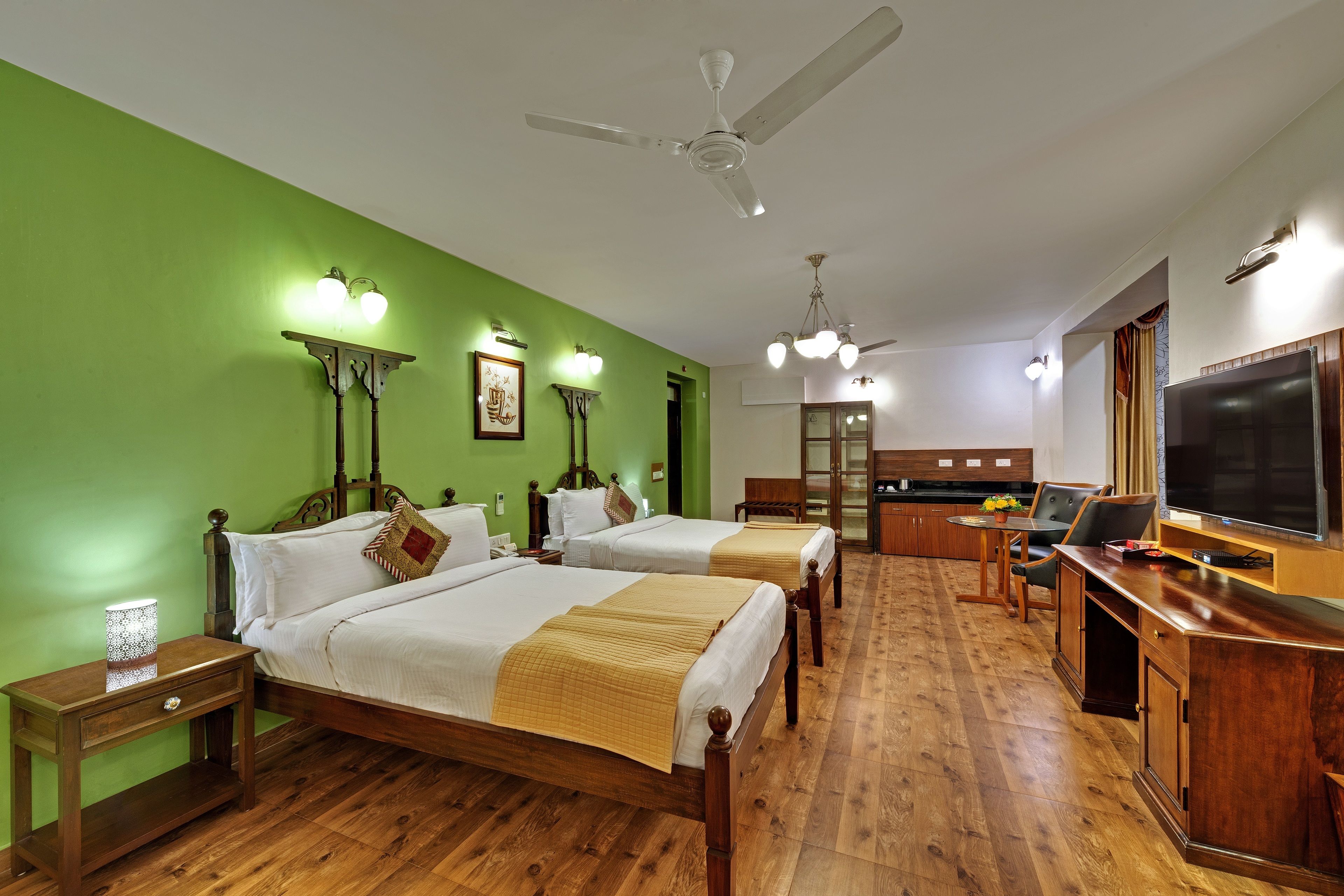 Een hotelkamer met twee bedden, een bureau, een televisie en een plafondventilator.