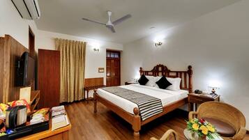 A hotel room with a wooden bed, a desk with a television, a chair, and a small table with flowers.
