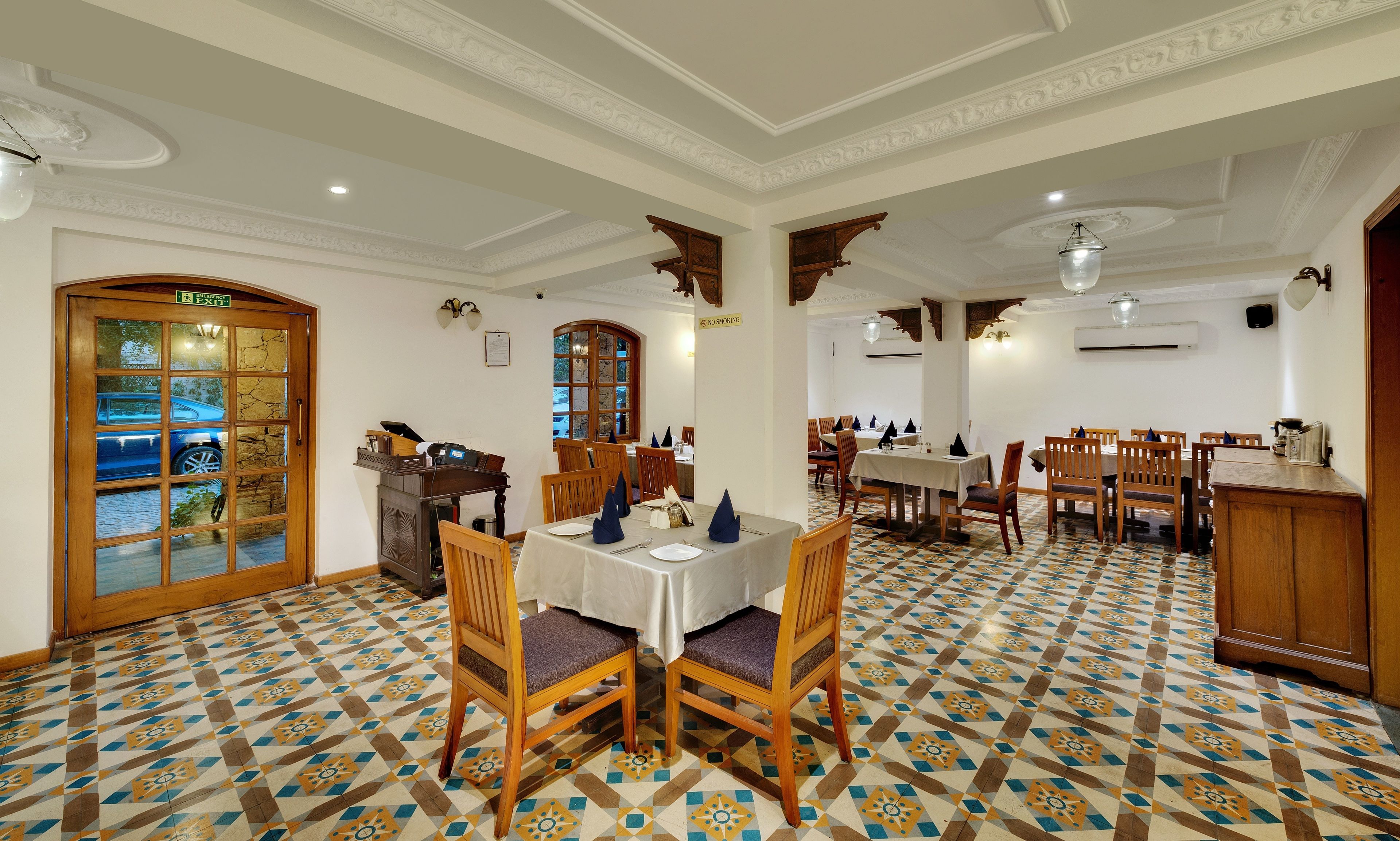 A dining area with patterned floor tiles, wooden chairs, and tables set for dining.