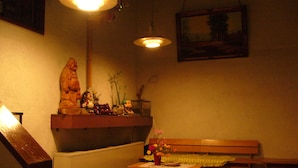 A dimly lit room with a wooden bench, a small table with a vase of flowers, and a statue on a shelf. - Hotel Senke (Myoko)