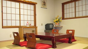 A traditional Japanese room with tatami flooring, a low table, wooden chairs, a television, and a vase with flowers. - Hotel Senke (Myoko)