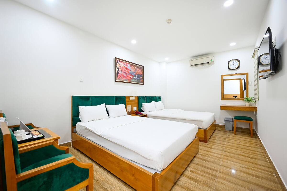 Une chambre d’hôtel avec deux lits, un bureau avec une chaise, une petite table sur laquelle se trouve un plateau avec divers objets, un miroir et une horloge murale.