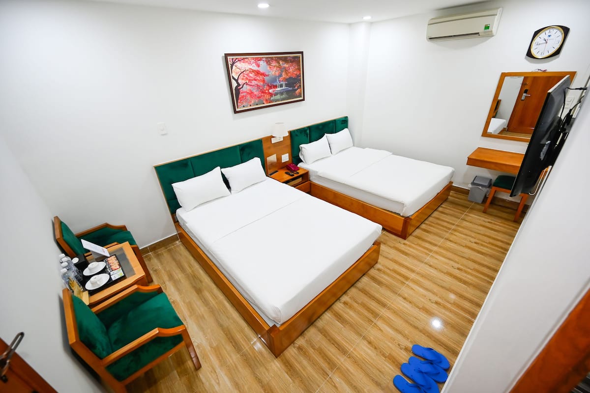 Une chambre d’hôtel avec deux lits, un bureau, une chaise, un miroir et une horloge au mur.
