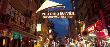 Escena callejera concurrida con diversos comercios y restaurantes, incluyendo un cartel llamativo que dice 'BUI VIEN WALKING STREET'.