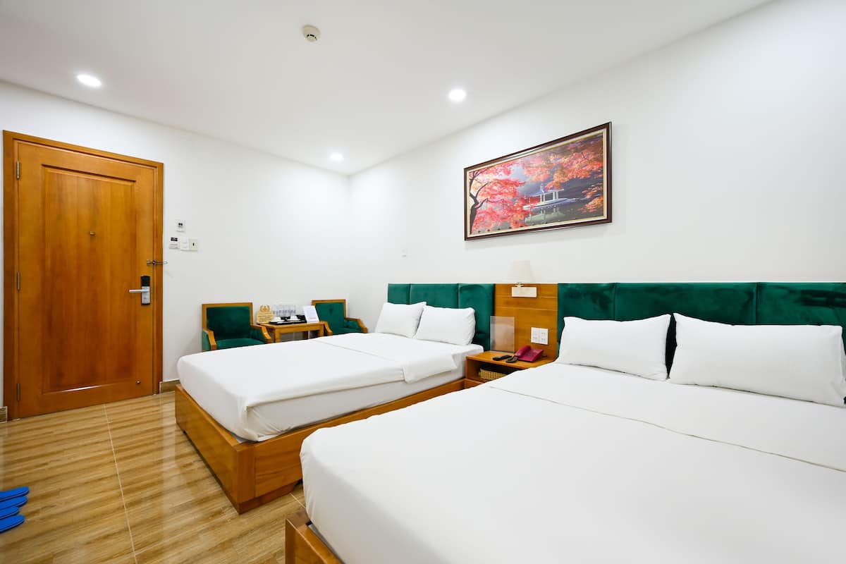 Une chambre d’hôtel avec deux lits, une tête de lit recouverte d’un tissu vert, un tableau représentant un arbre et une porte en bois.