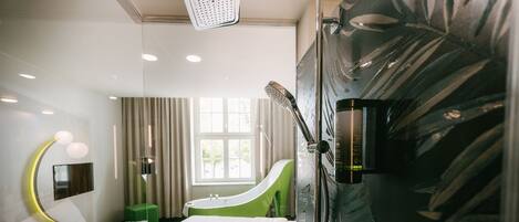 A modern bathroom with a shower, a green bathtub, a vanity with a mirror, and a large window providing natural light.