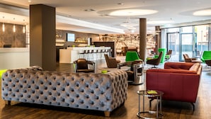 A modern hotel lobby with a reception desk, seating area, and bar. - Travel24 Hotel (Leipzig)