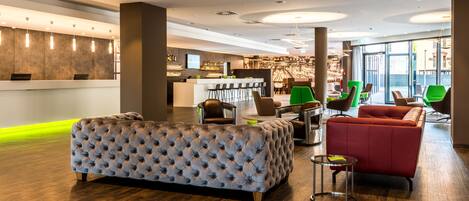 A modern hotel lobby with a reception desk, seating area, and bar.