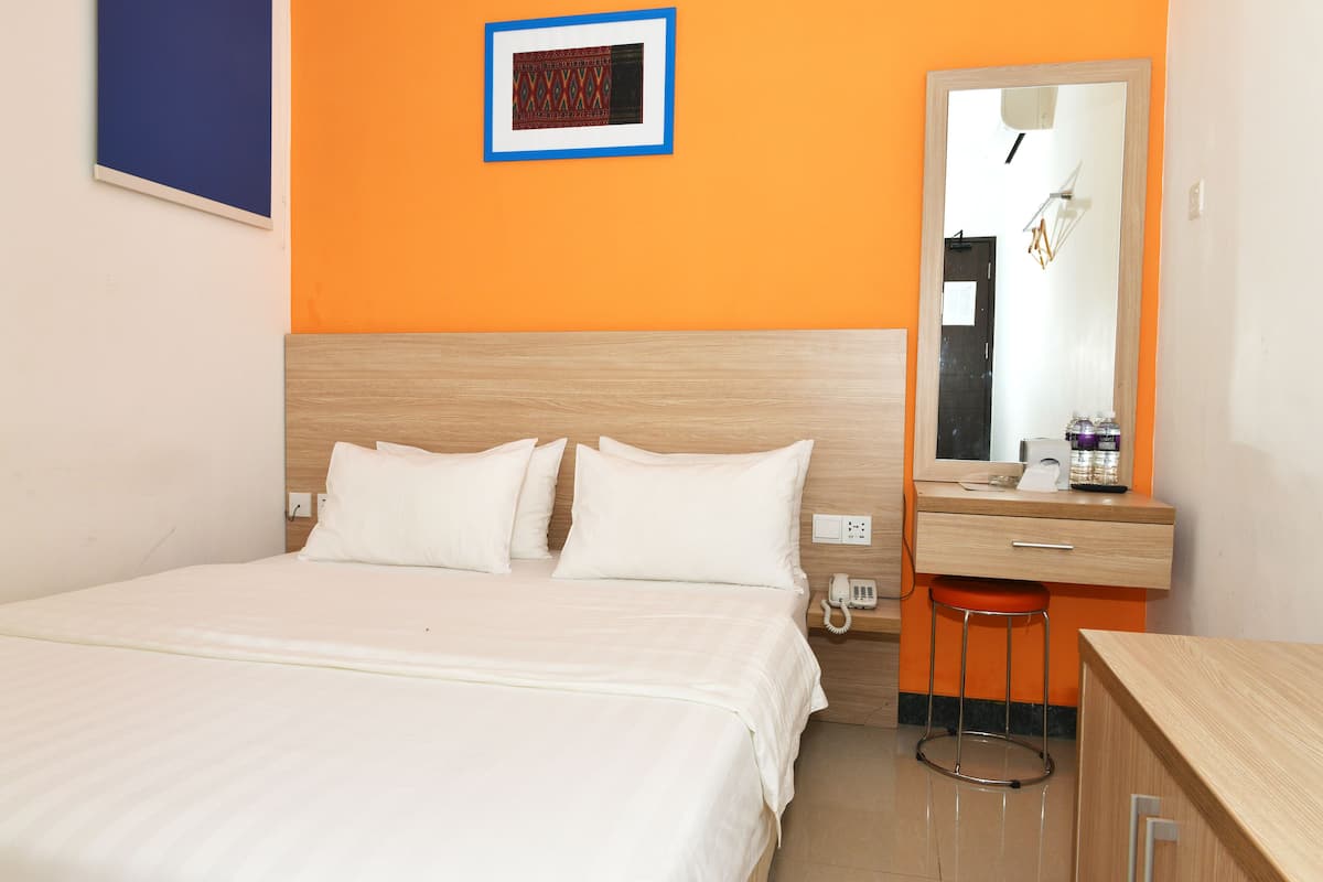 A hotel room with a bed, a bedside table with a phone, a mirror, and a small stool.