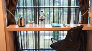 Une chambre d’hôtel avec un bureau en bois, une chaise noire, une bouilloire, deux bouteilles d’eau, un bocal en verre et une télécommande.
