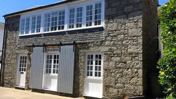 A two-story stone building with a flat roof, large windows on the upper floor, and a door on the ground floor.