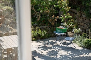 Een terras met een tafel en stoelen, een stenen muur en weelderige begroeiing.