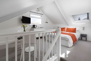 Un dormitorio en el ático con una cama, un escritorio, una silla, un televisor y una ventana.