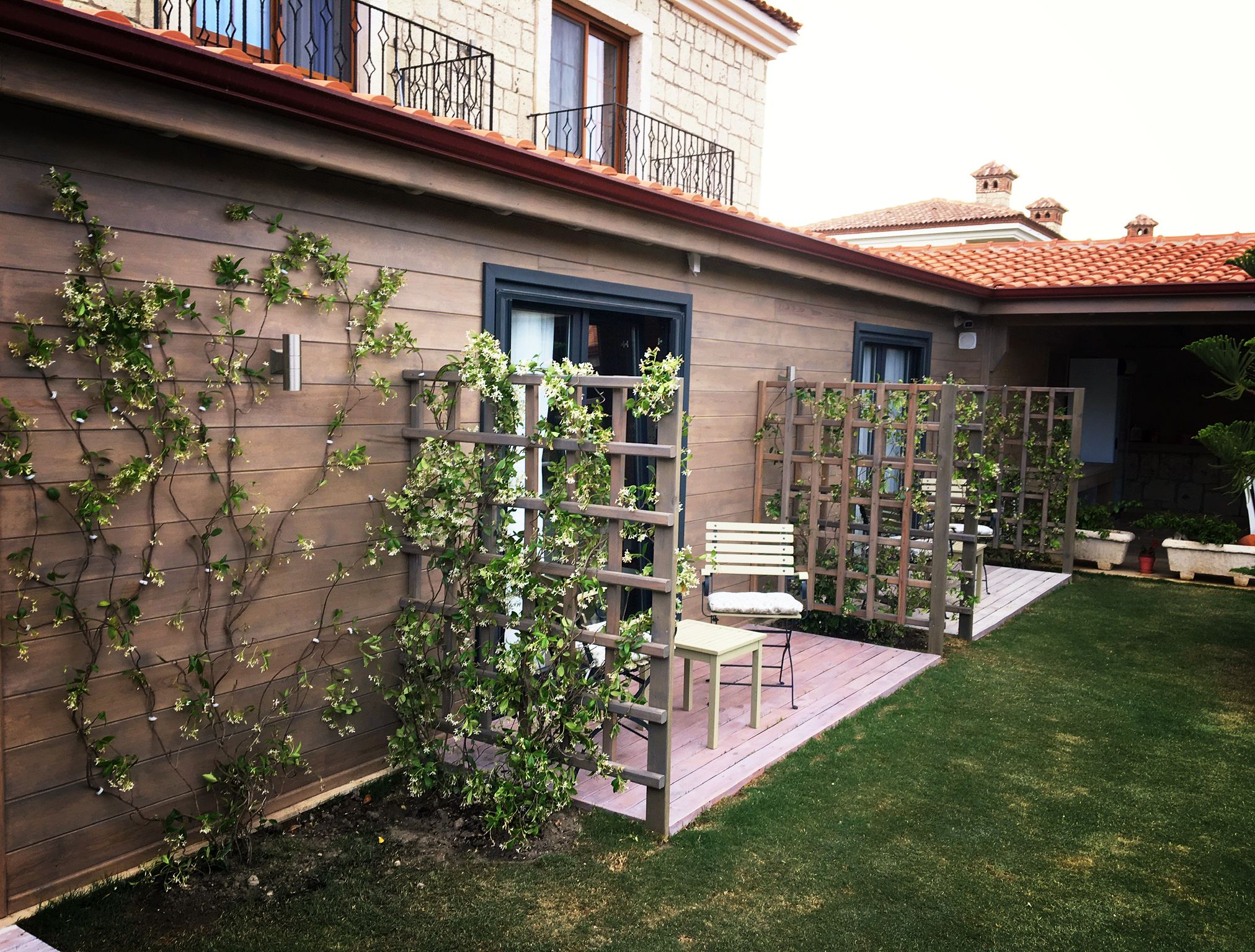 Een woongebouw met een houten terras, een witte bank en een tuin met klimplanten.