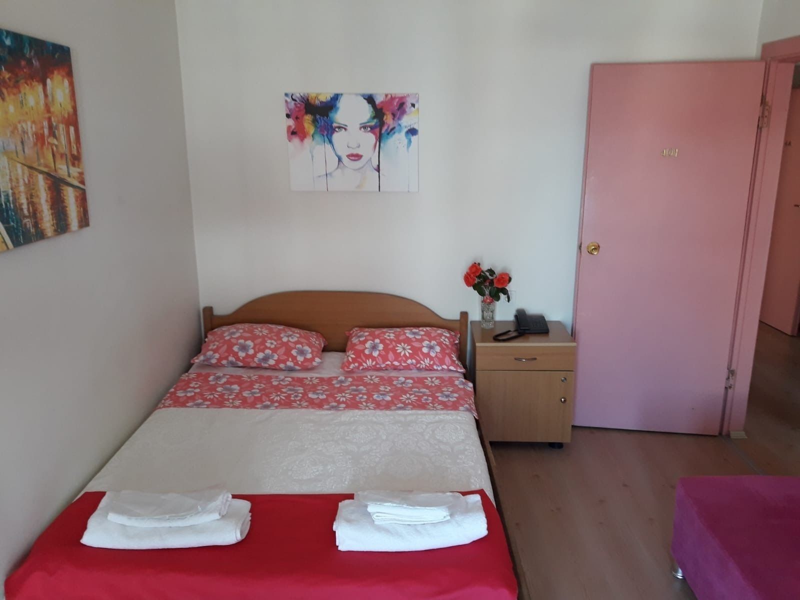 Un dormitorio con cama, mesita de noche, un florero con flores y una puerta.