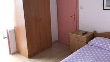 A bedroom with a bed, a wooden wardrobe, a pink door, a bedside table with a remote control, and a framed picture on the wall.