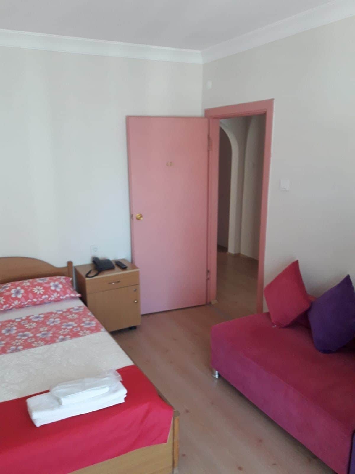 A bedroom with a bed, a nightstand, a pink door, and a red sofa.