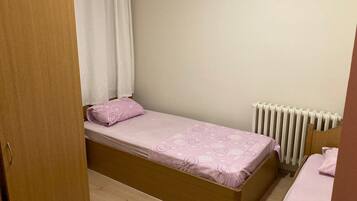 Una habitación pequeña con una cama individual, estructura de madera, radiador blanco y puerta de madera.