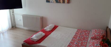 Een slaapkamer met een bed, een radiator, een schilderij en een televisie.