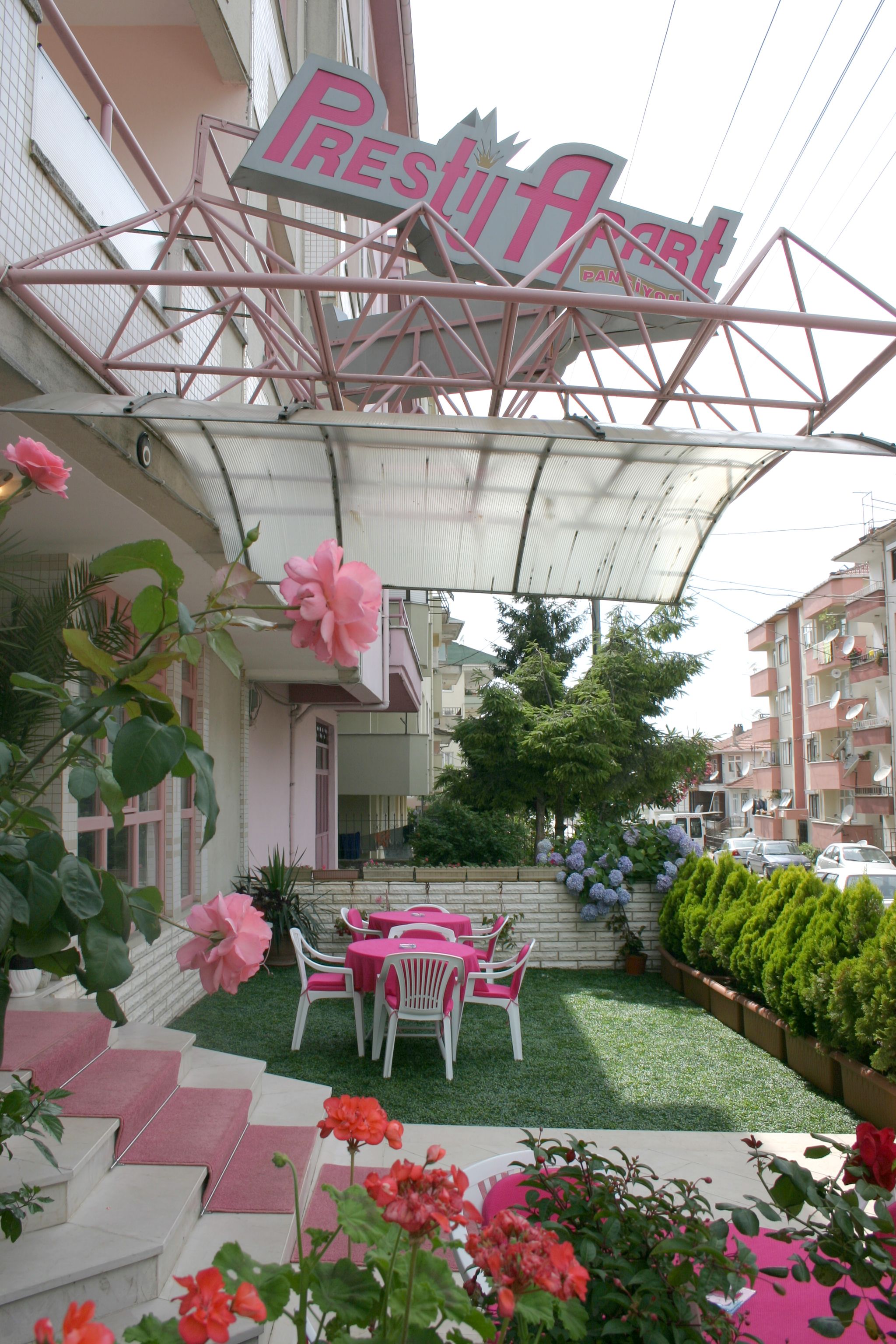 Een restaurant met een roze bord, terras en een bloemen tuin.