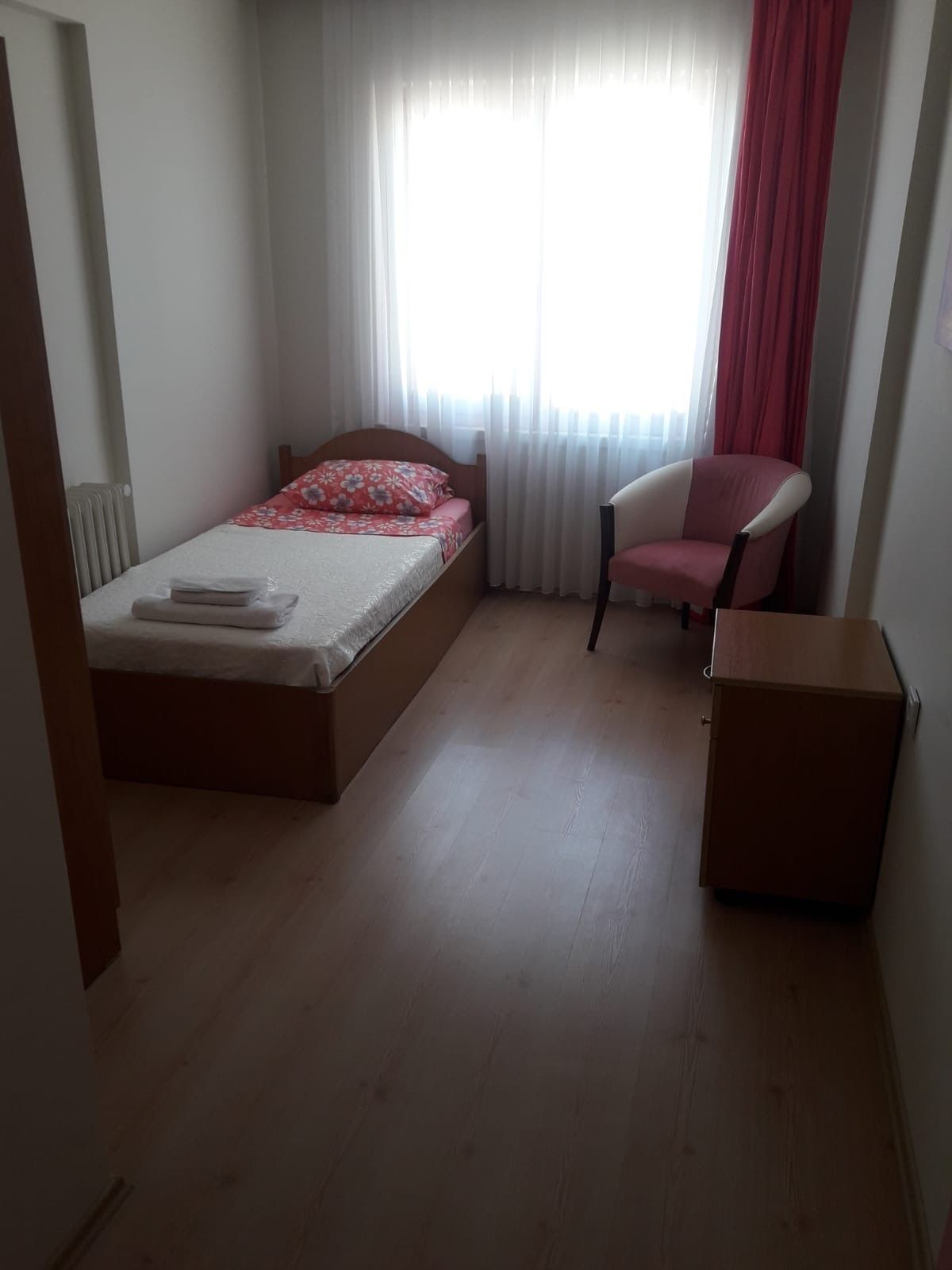 A bedroom with a bed, a chair, a cabinet, and a window with curtains.