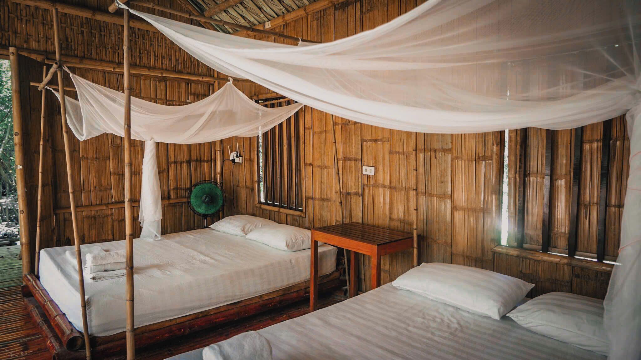 A room with two beds, one with a canopy and a green fan, and wooden walls.