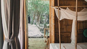 Een bamboe hut met rieten dak, een houten vloer en een bed met hemelbed.