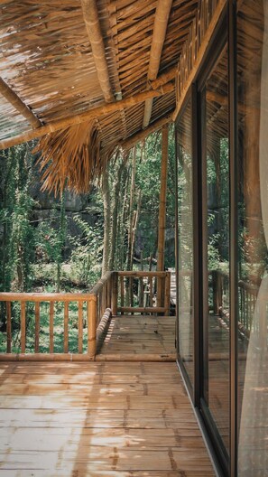A wooden deck with a thatched roof, surrounded by glass walls offering views of a forested area. - Chez Beo Homestay (Nam Hoa Lu)