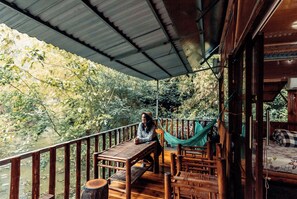 Une terrasse en bois avec une table et des chaises, donnant sur une rivière bordée d’arbres.