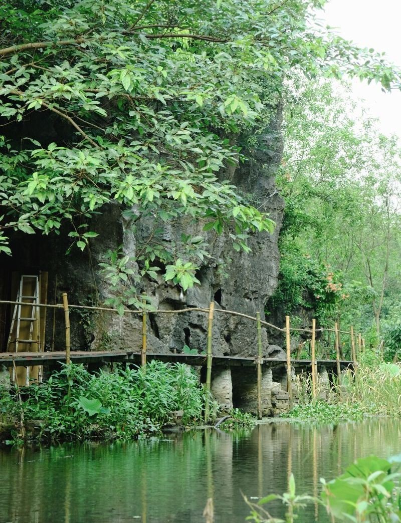 A natural rock formation with a wooden bridge over a calm body of water, surrounded by lush greenery.