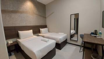 Habitación de hotel con dos camas, un escritorio, una silla, un ventilador de techo y un espejo.