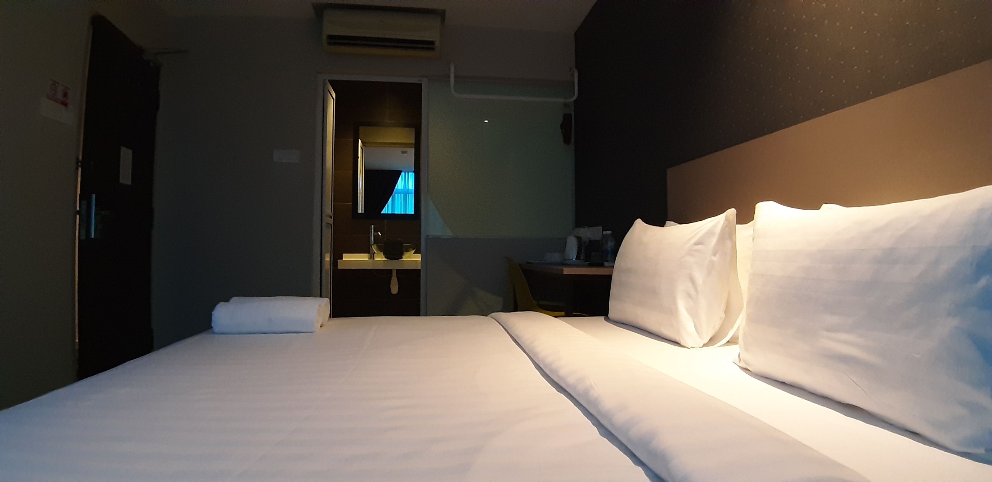 A hotel room with a neatly made bed, a bedside table, a small desk, and a mirror.