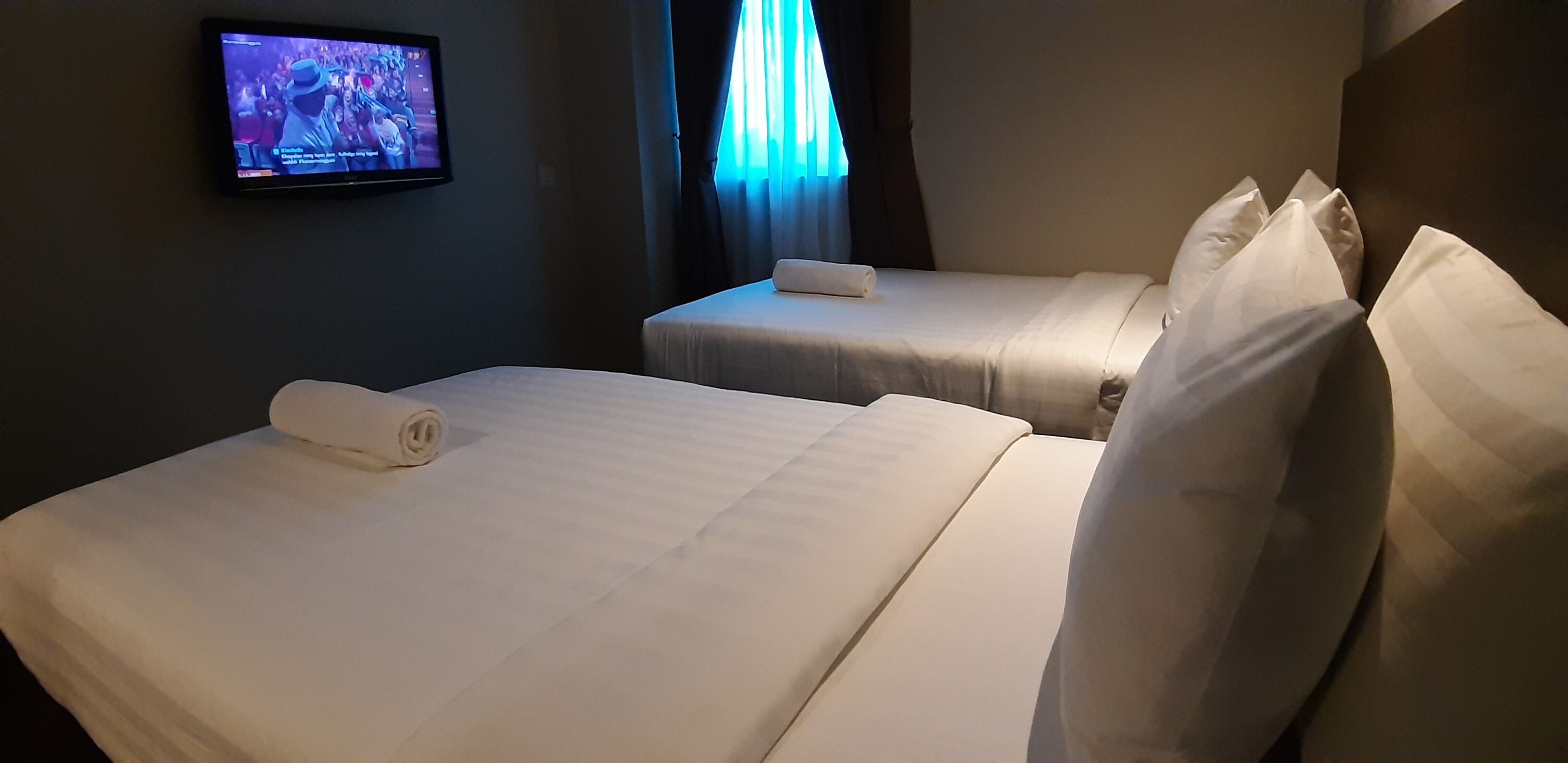 A hotel room with two beds, a TV on the wall, and a window with curtains.