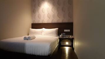 A neatly made bed with white linens and rolled towels, a bedside table with a lamp, and a wall with a leaf pattern.