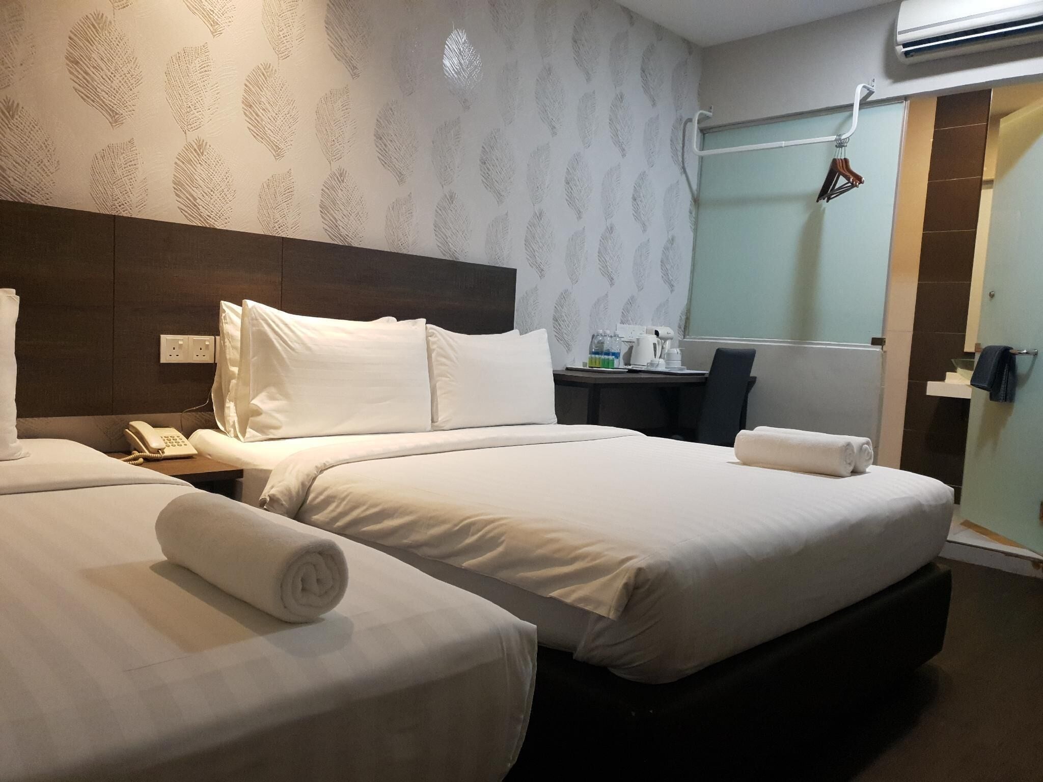 A hotel room with two beds, a desk, a telephone, and an air conditioning unit.