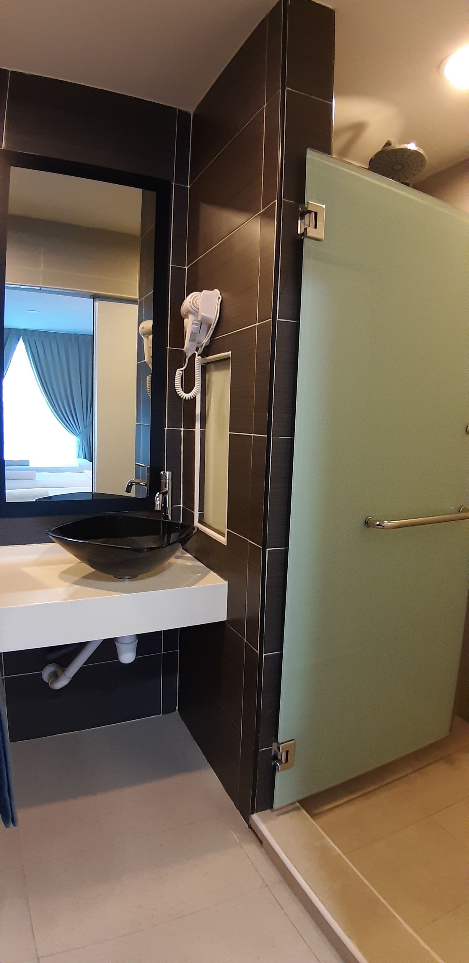 A bathroom with a black and white tiled wall, a white sink with a black bowl, a hairdryer, and a mirror.