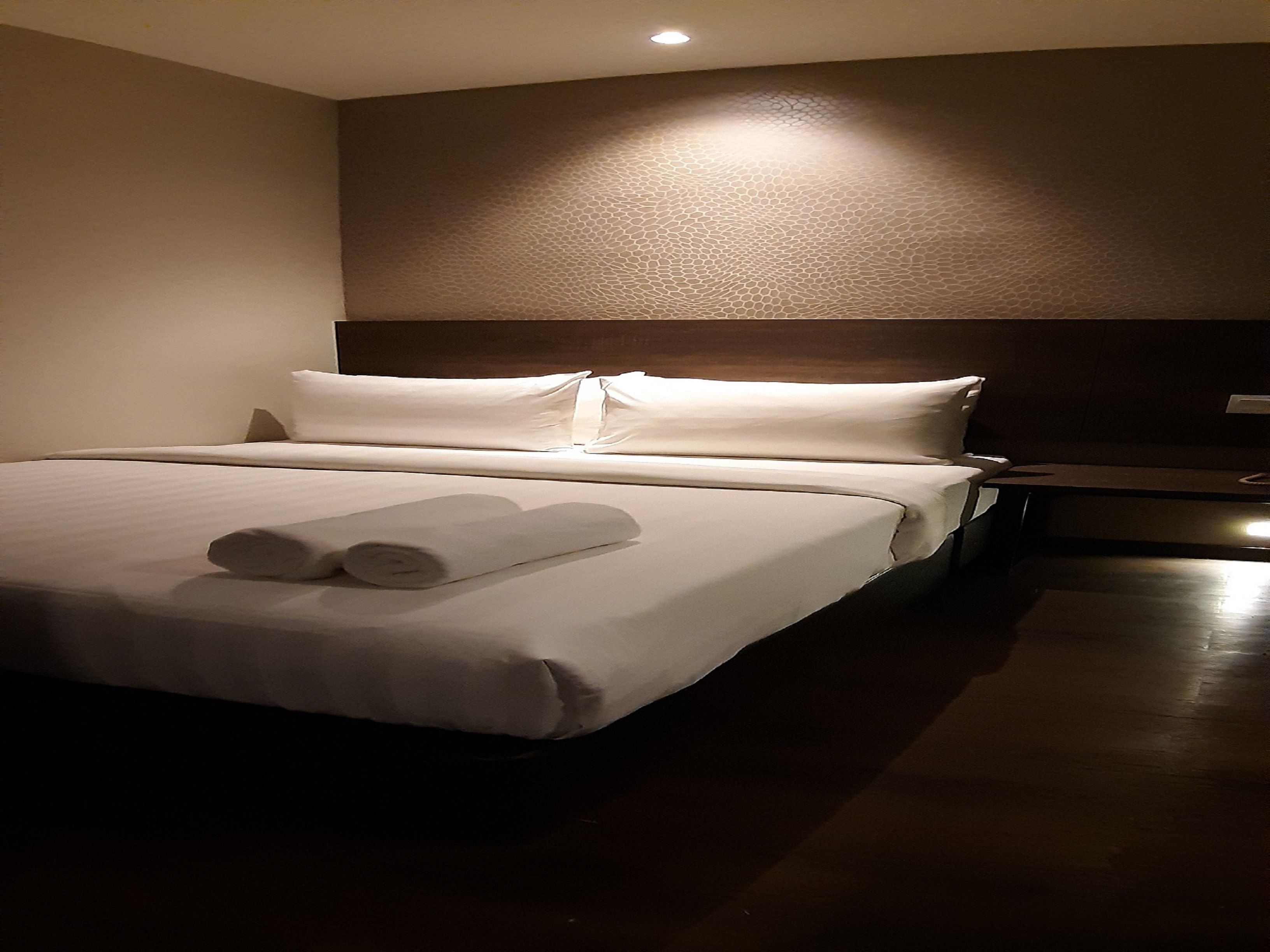 Una habitación de hotel con una cama bien hecha, un cabecero de madera y una mesita de noche pequeña.