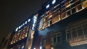 Hotel com fachada moderna, sinalização iluminada e varanda com ripas verticais.